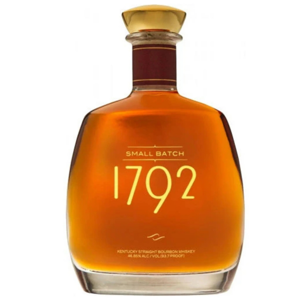 A bottle of 1792 Small Batch Bourbon displayed on a wooden table, surrounded by a tumbler glass filled with bourbon and a garnish of orange peel, evoking a sense of refined craftsmanship and rich flavor.