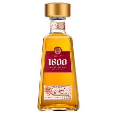 A bottle of 1800 Reposado Tequila with its golden amber color, placed on a wooden surface, accompanied by a glass filled with tequila and lime wedges.