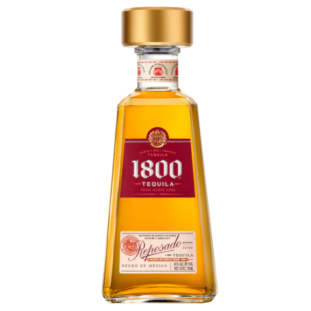 A bottle of 1800 Reposado Tequila with its golden amber color, placed on a wooden surface, accompanied by a glass filled with tequila and lime wedges.