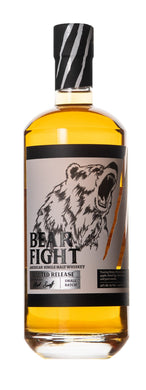 A bottle of Bear Fight American Single Malt Whiskey sitting on a rustic wooden table, surrounded by oak barrels.  